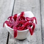 Gusanos y sanguijuelas de gominola caseros de color rojo oscuro, amontonados en un cuenco blanco sobre una mesa de madera.