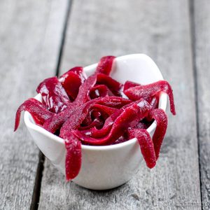 Gusanos y sanguijuelas de gominola caseros de color rojo oscuro, amontonados en un cuenco blanco sobre una mesa de madera.