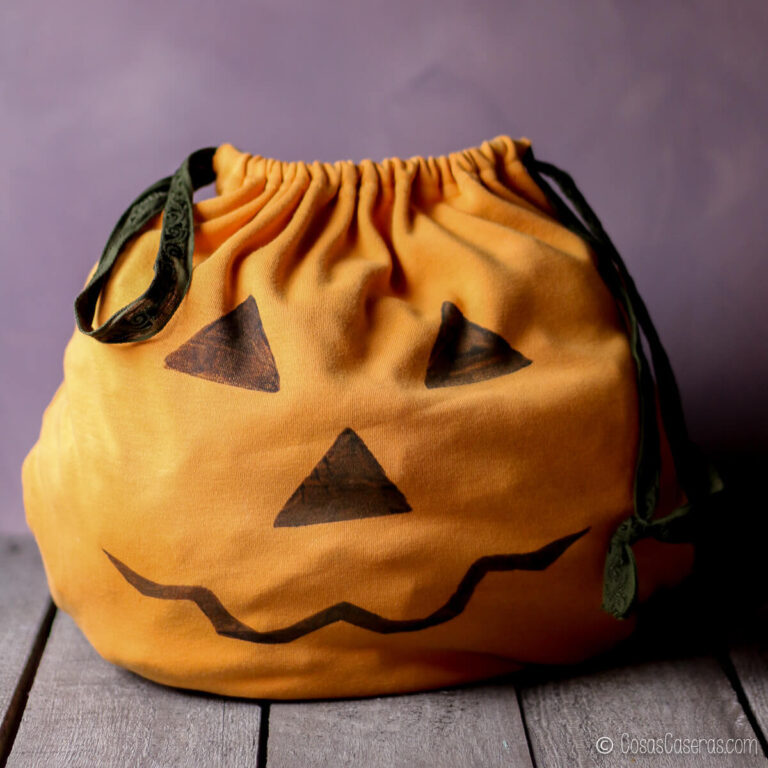 Bolsa naranja con cordón para «truco o trato», decorada con una cara de calabaza de Halloween negra.