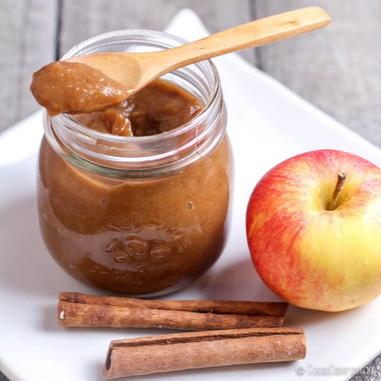 Tarro de mantequilla de manzana casera con una cuchara de madera, una manzana y ramas de canela.