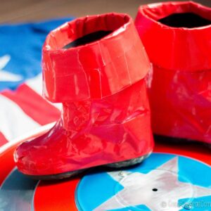 Un par de botas rojas hechas con cinta adhesiva para un disfraz casero, apoyadas sobre el escudo del Capitán América.