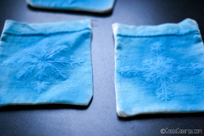2 bolsitas de tela pintadas de azul por encima de los copitos de nieve de papel 