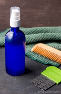 Una botella con un spray repelente de piojos, al lado de un peine de madera y un peine de liendres.