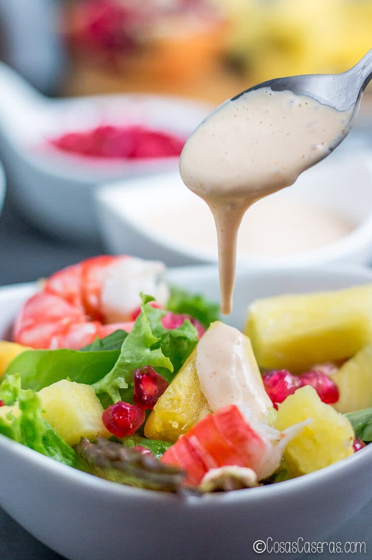 Echando un poco de salsa rosa encima de una ensalada con gambas y fruta