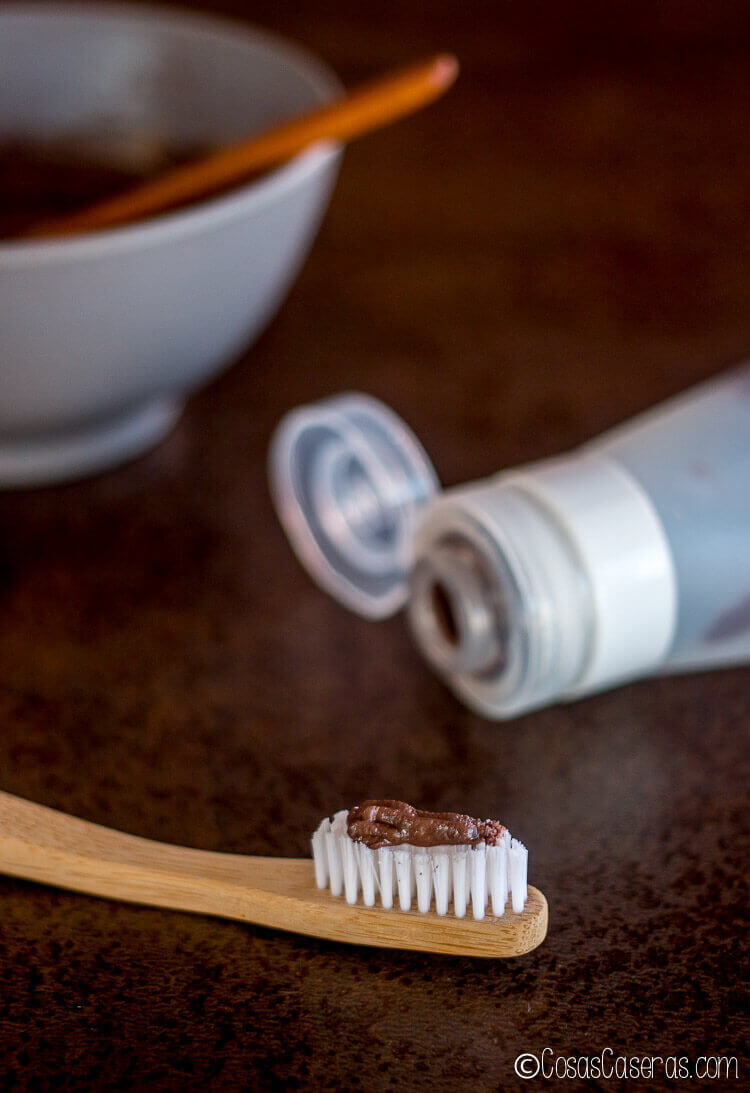Pasta de dientes casera de chocolate y menta en un cepillo de dientes de bambú y con un tubo silicona llena de la pasta de dientes.