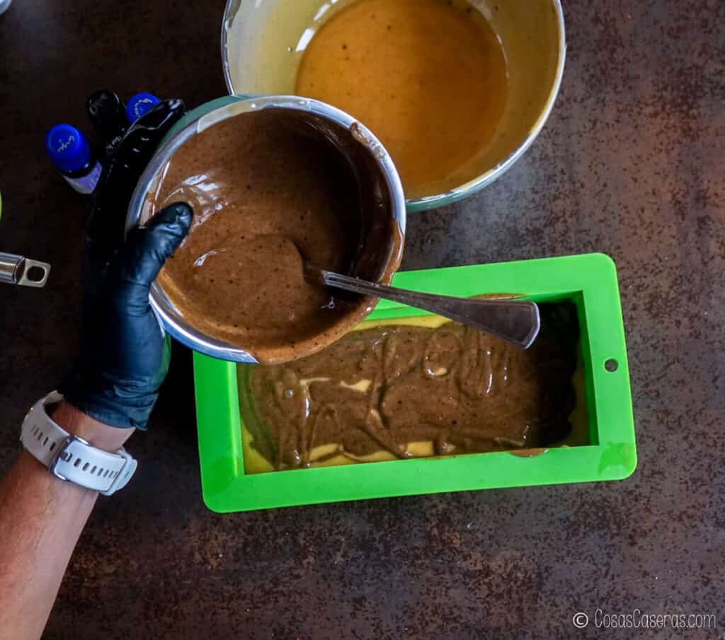 Echando una mezcla de jabón de color marrón sobre uno de color dorado en un molde de silicona