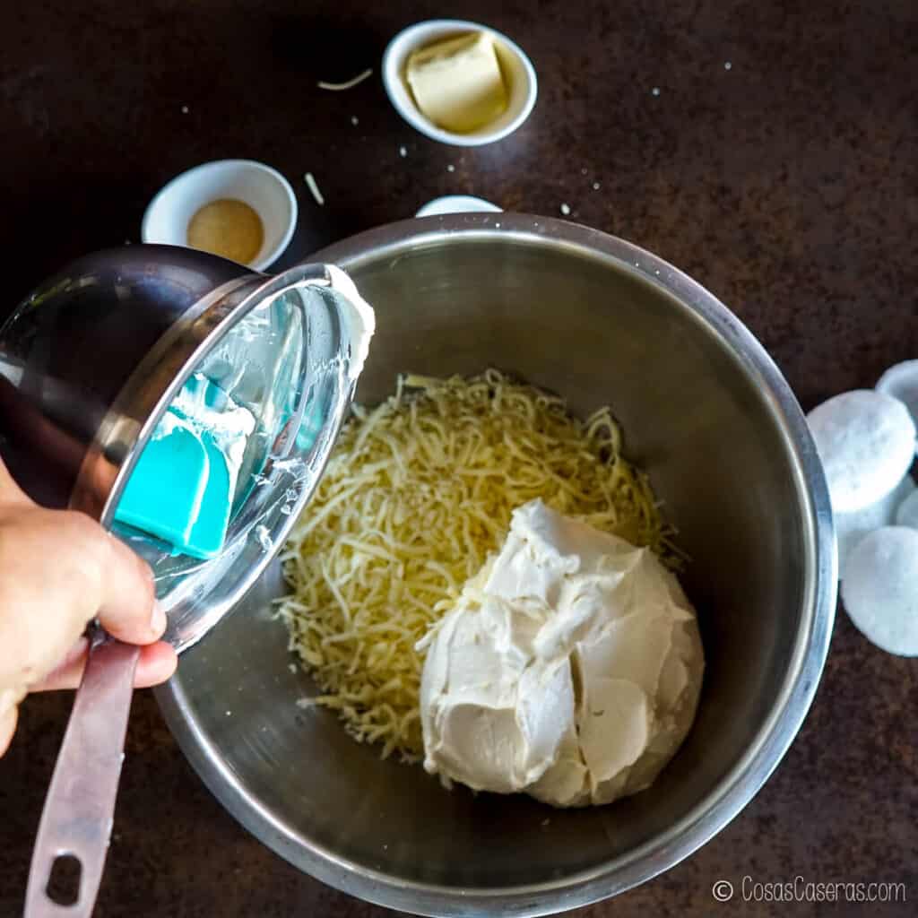 Agregando la crema de queso a un bol con quesos rallados