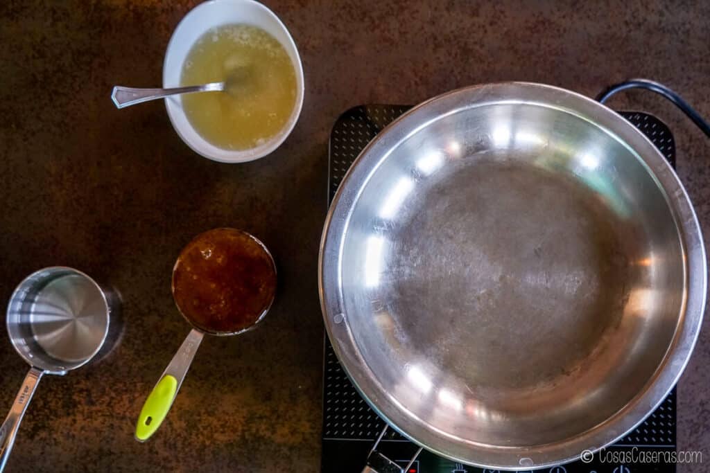 Vista aérea de una cacerola vacía con una taza de miel a la izquierda y una mezcla de gelatina y agua en un recipiente encima.