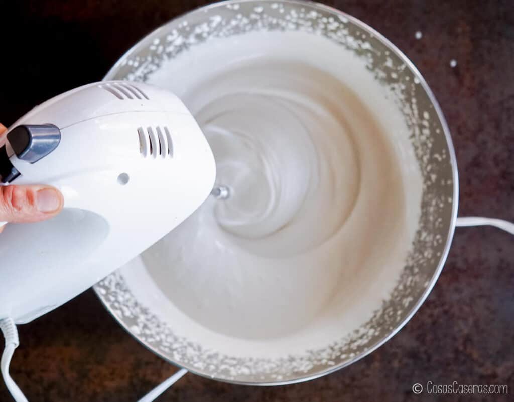 Vista aérea de una batidora eléctrica batiendo la mezcla de gelatina con miel. Ha aumentado de volumen y es de color blanco.