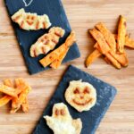 Dos platos de pizarra sobre una mesa de madera, cada uno con nuggets de pollo en forma de cara sonriente y una porción de batatas fritas.