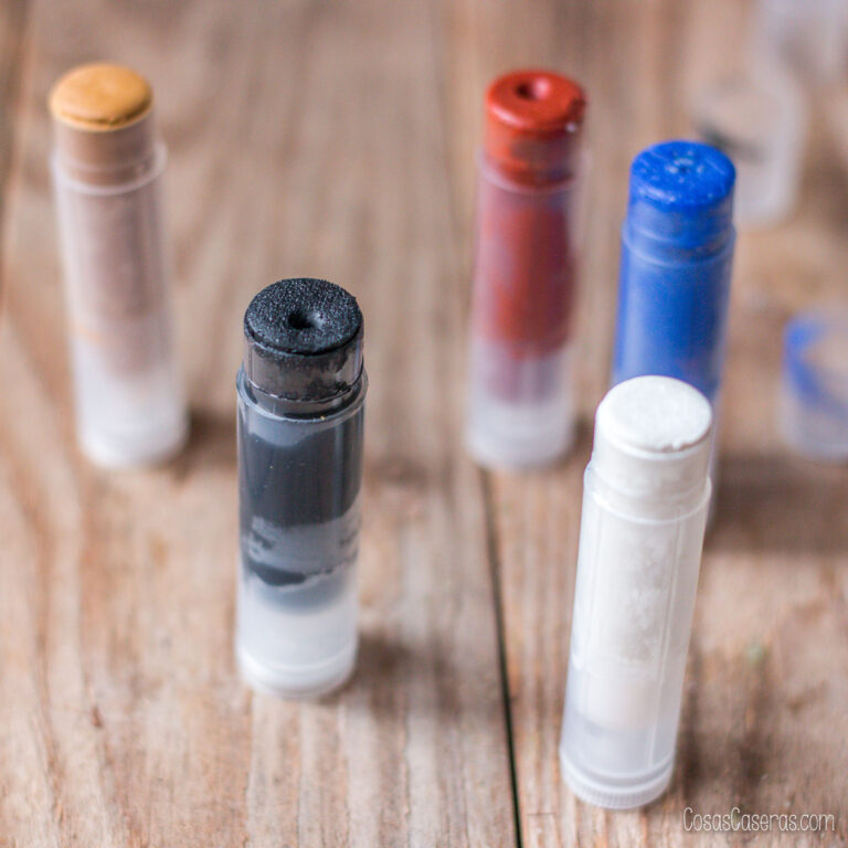 Cinco barras de maquillaje casero para disfraces de Halloween en tonos negro, blanco, rojo, azul y beige, sobre una mesa de madera.