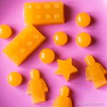 Gominolas caseras de color naranja con formas de piezas y figuras LEGO, estrellas y círculos, sobre un fondo rosa.