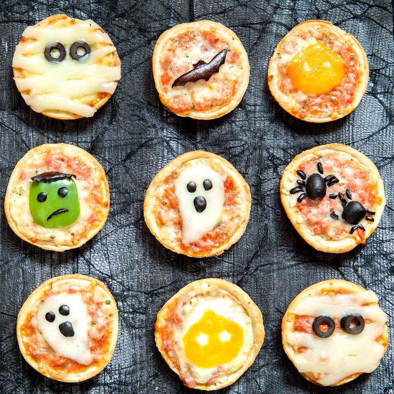 Nueve minipizzas decoradas con motivos de Halloween, como momias, un fantasma, arañas y calabazas de Halloween, dispuestas en forma de cuadrícula.