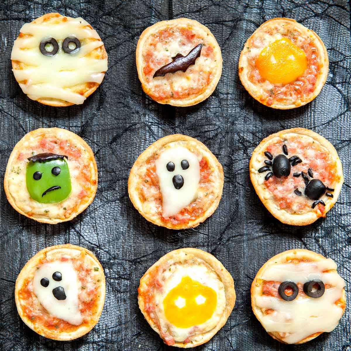 Nueve minipizzas decoradas con motivos de Halloween, como momias, un fantasma, arañas y calabazas de Halloween, dispuestas en forma de cuadrícula.