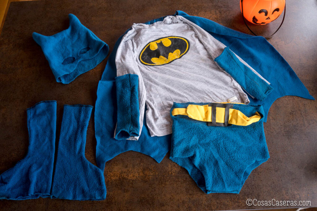Disfraz casero de Batman con camiseta gris, capa azul de tela polar, máscara con orejas puntiagudas, guantes sin dedos, botas y calzoncillos con cinturón amarillo.